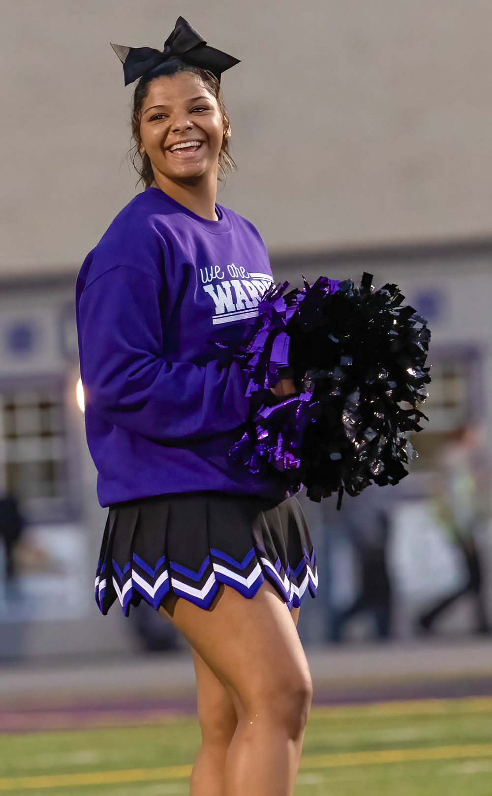 Cheerleader in purple sweatshirt and black bow holds black and purple pom poms while performing at sporting event.
cheer kanawha county rive
