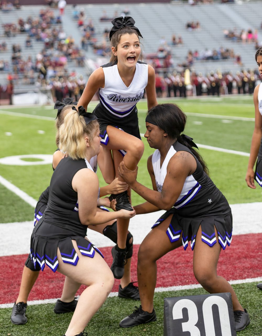 Cheerleaders execute a complex stunt formation on football field during game.
cheer kanawha county riverside