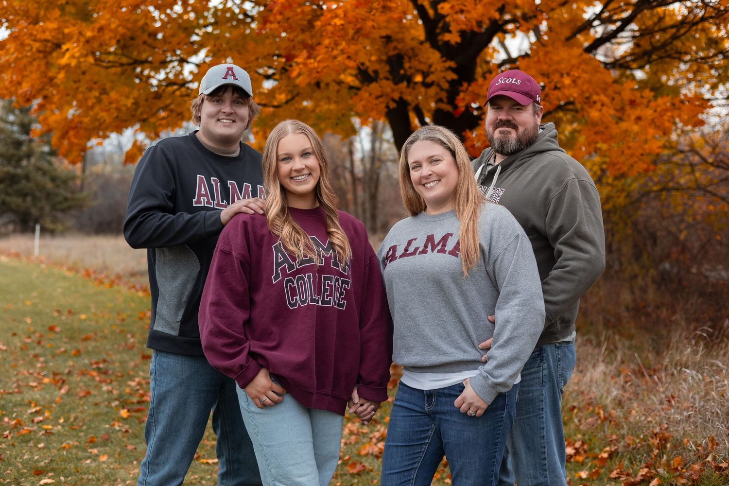 Group poses together outdoors surrounded by vibrant orange autumn foliage on a fall day.