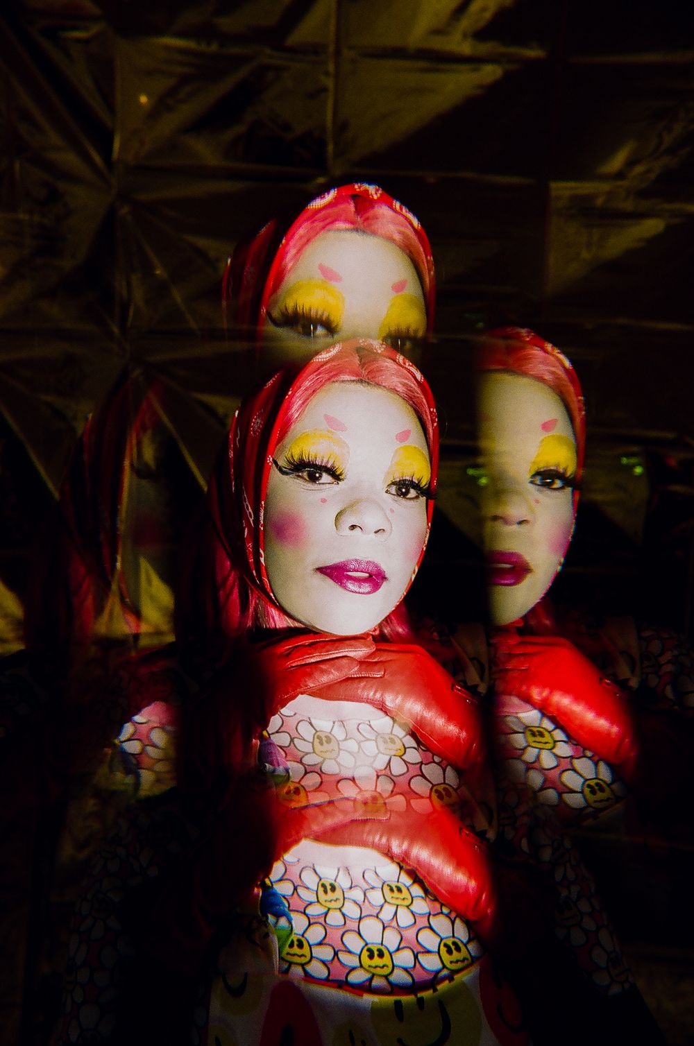 Multiple reflections create dramatic portrait with red lighting and bold makeup.