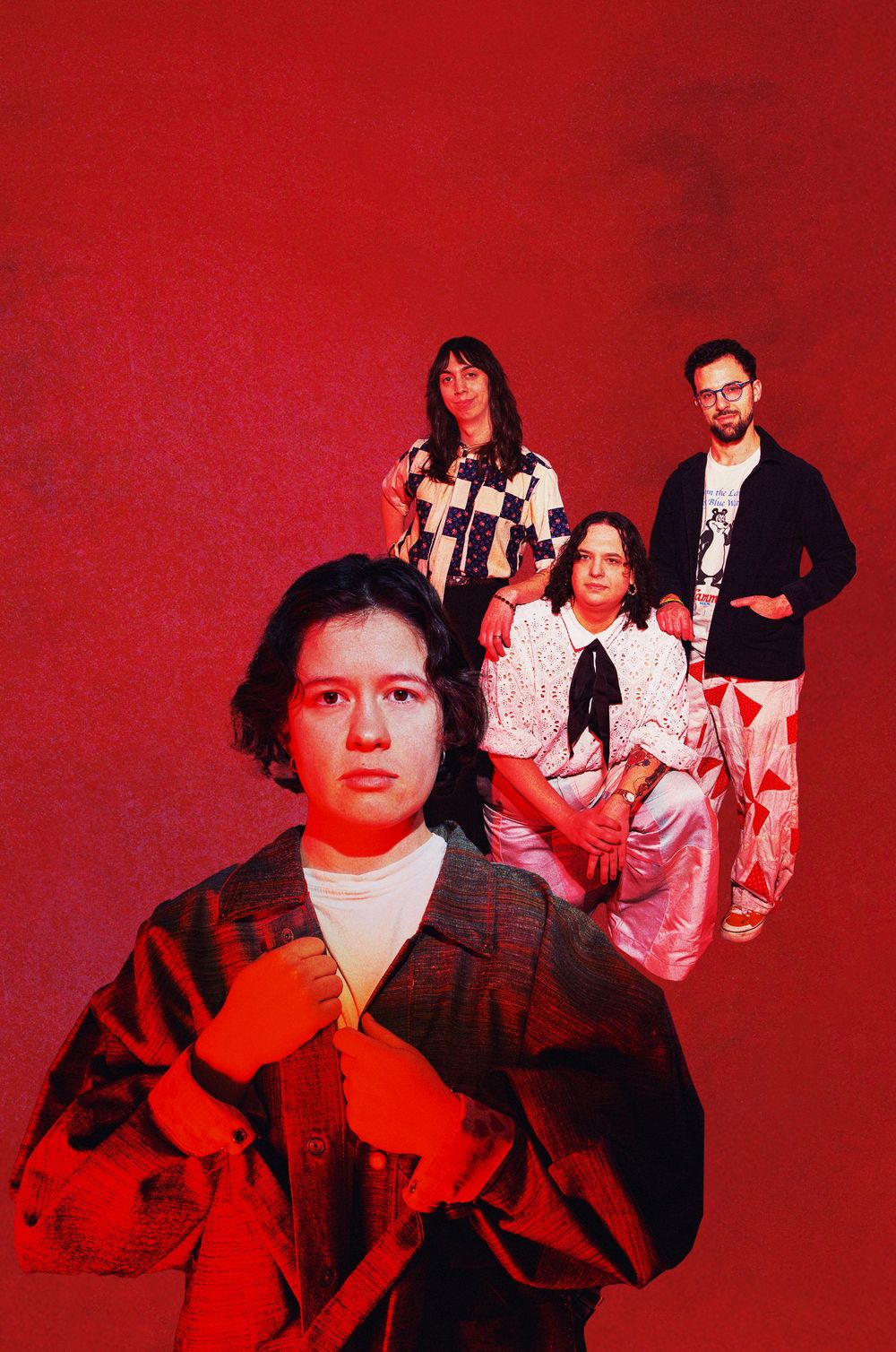 Four young adults pose against a bold red background in stylish, eclectic outfits for a creative band or group photo.