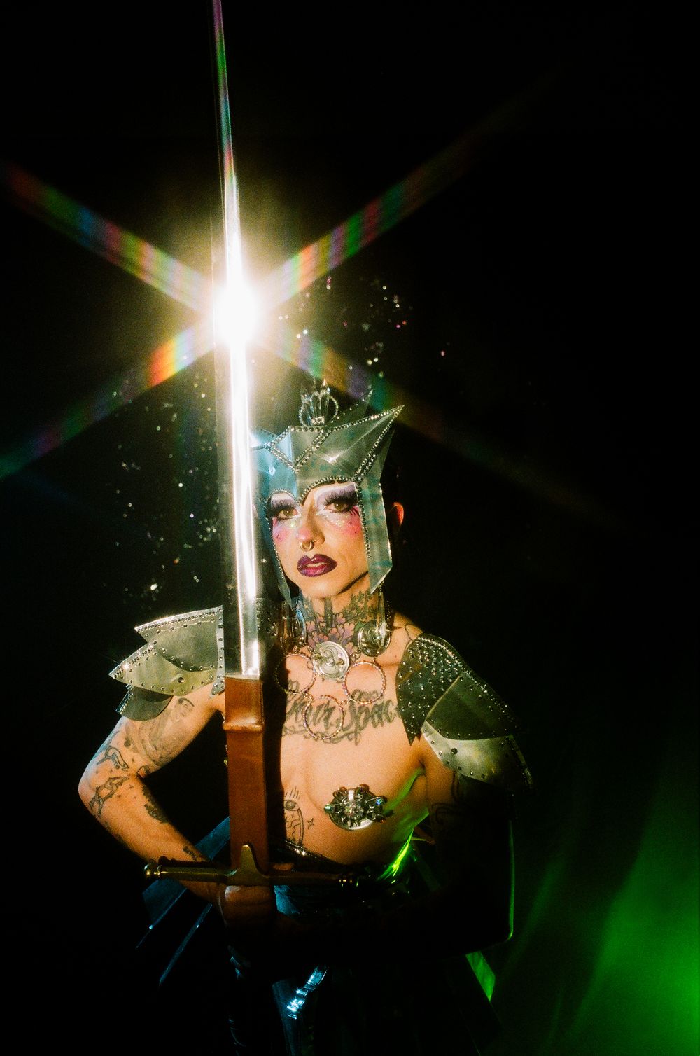 Burlesque performer with glittery costume holds illuminated sword on dark stage.