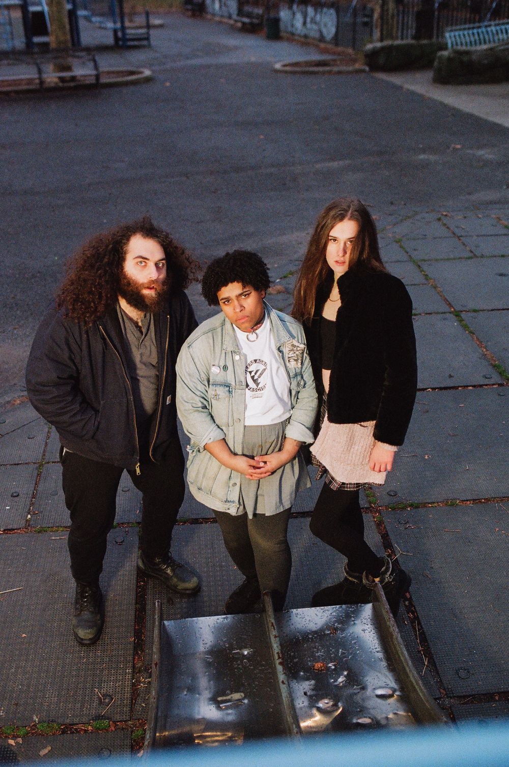 Three people sit together on a sidewalk in casual clothing at dusk.