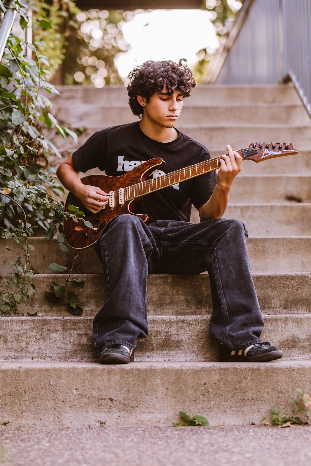 A guitarist in dark clothing sits on concrete steps playing an electric guitar in a series of progressive shots.