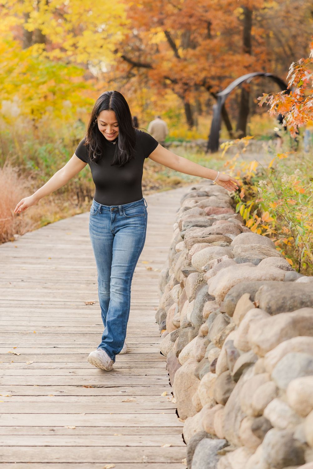 Someone in casual attire walking playfully along wooden boardwalk surrounded by fall colors.