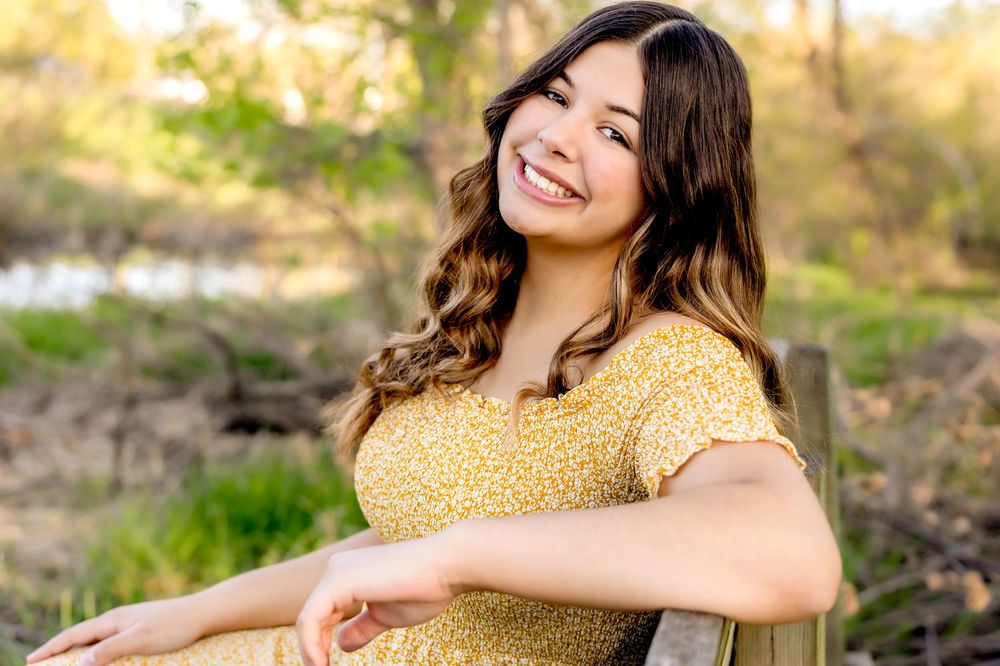 Person wearing yellow polka dot dress sits outdoors with warm autumn lighting in a natural setting.