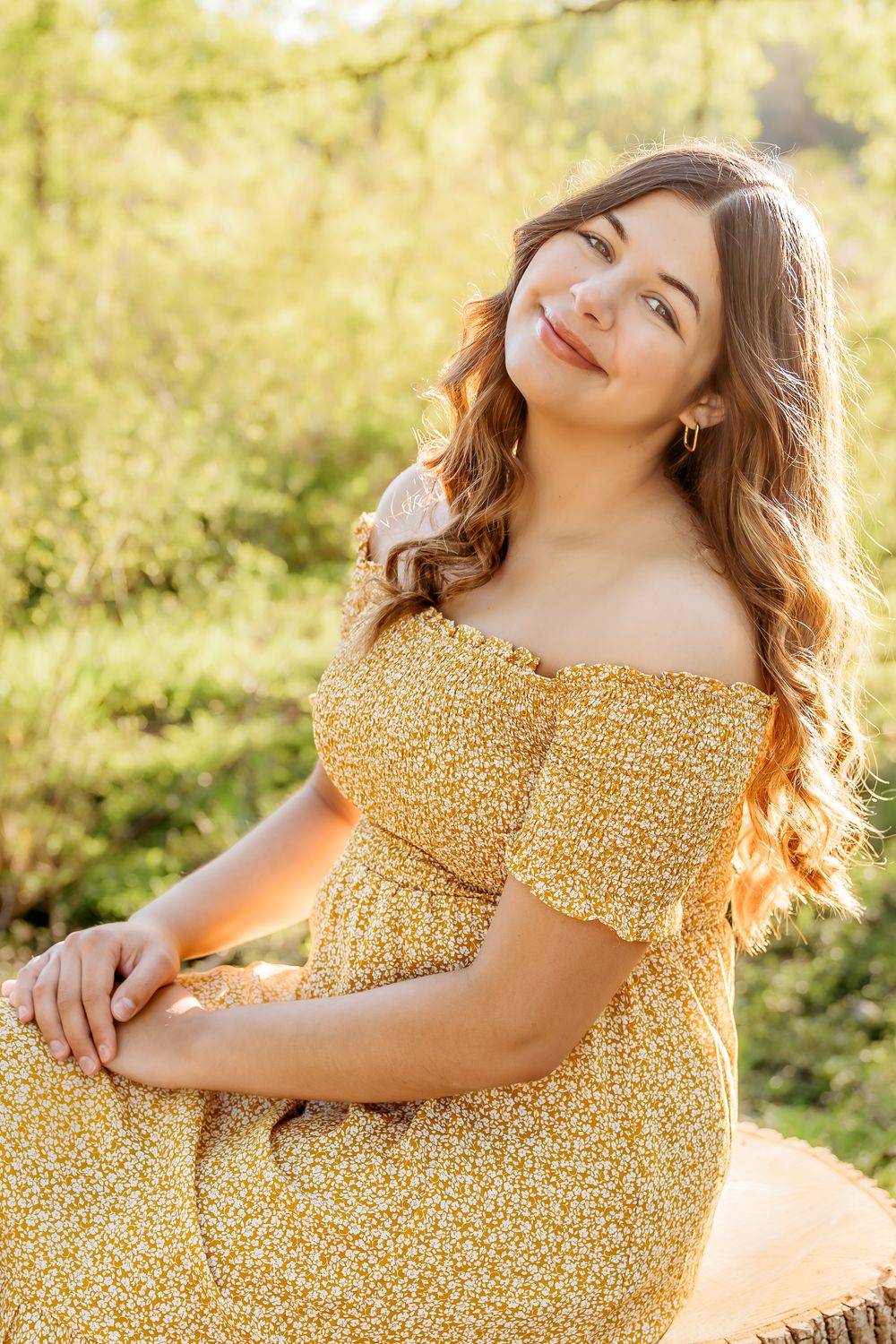 A woman in a yellow floral dress sits peacefully outdoors during golden hour with soft natural lighting.