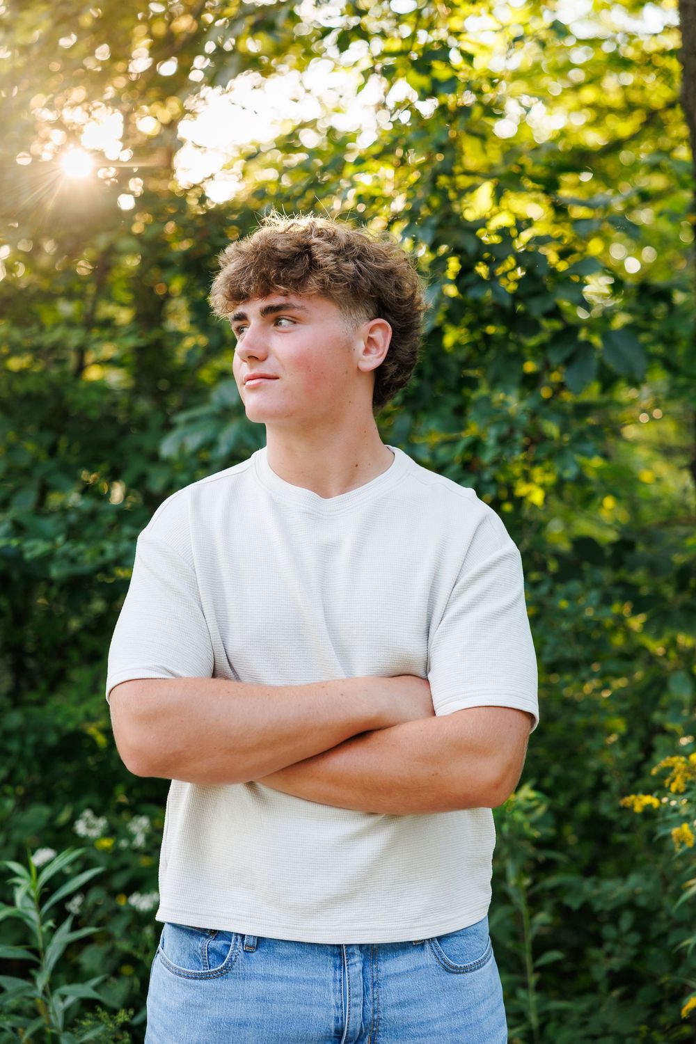 A person in white t-shirt and jeans stands against green foliage in a casual outdoor photoshoot series.