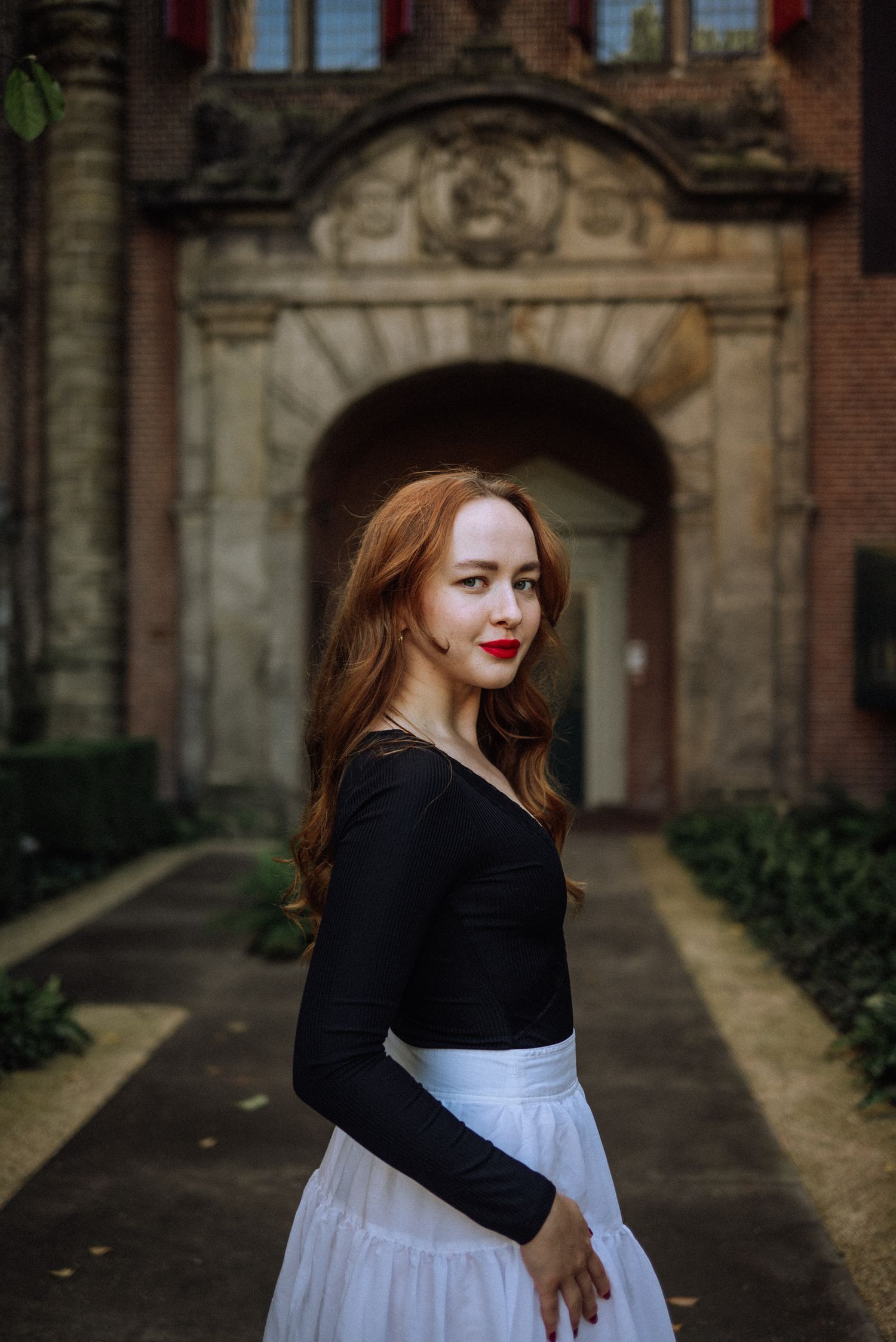 A red-haired woman in the Rijksmuseum garden looking directly into the camera during her solo session in Amsterdam.