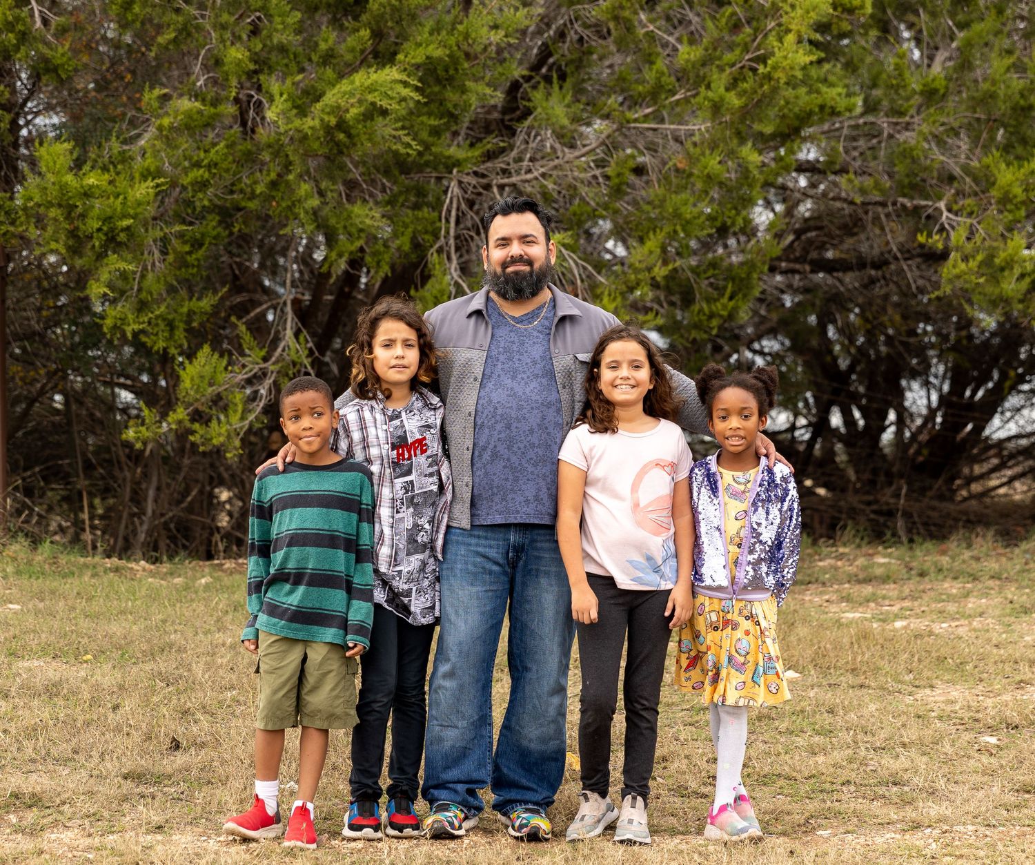 A family group poses together outdoors against a backdrop of evergreen trees.