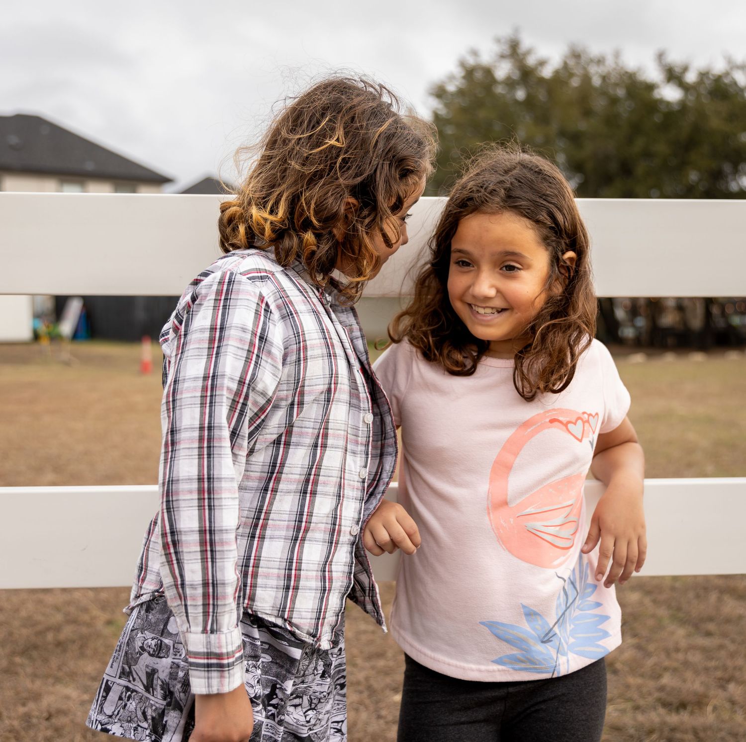 Two young people share a heartwarming moment while leaning against a white fence.