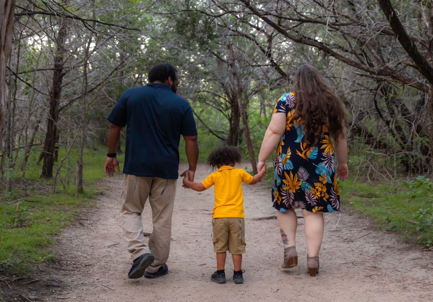 Rear view of trio walking hand in hand down nature trail surrounded by trees.