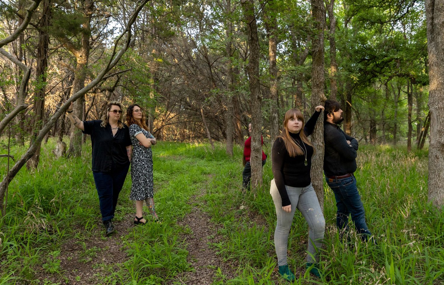 A group poses playfully in a wooded area with green grass and trees.