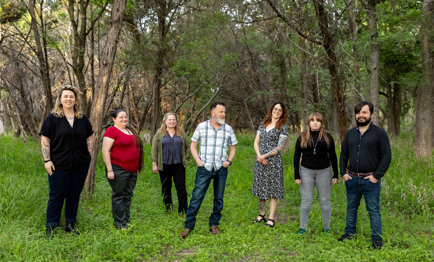 A casual group photo of people standing together in a natural outdoor setting with trees.