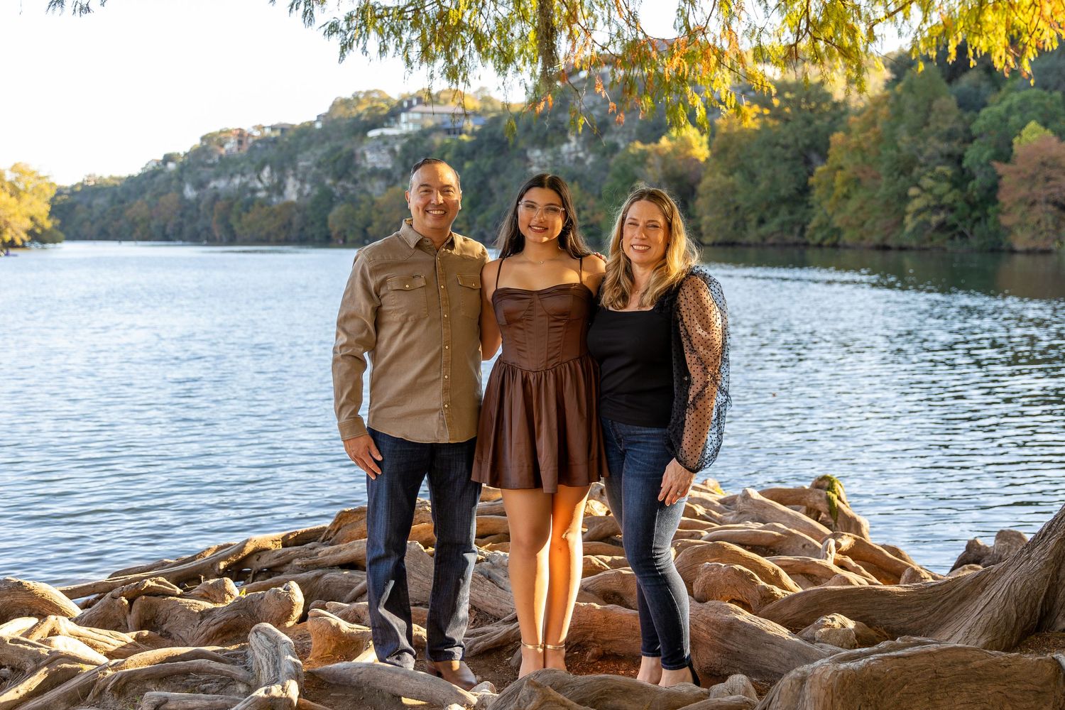 A group stands together on rocky shoreline during golden hour with autumn trees and lake in background.