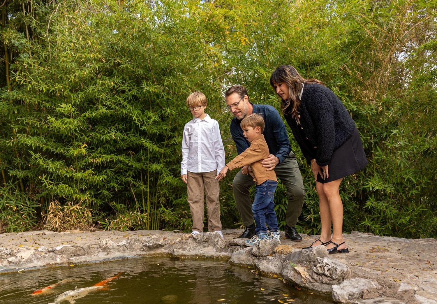 A group explores and examines rocks along the edge of a peaceful stream surrounded by lush green foliage.