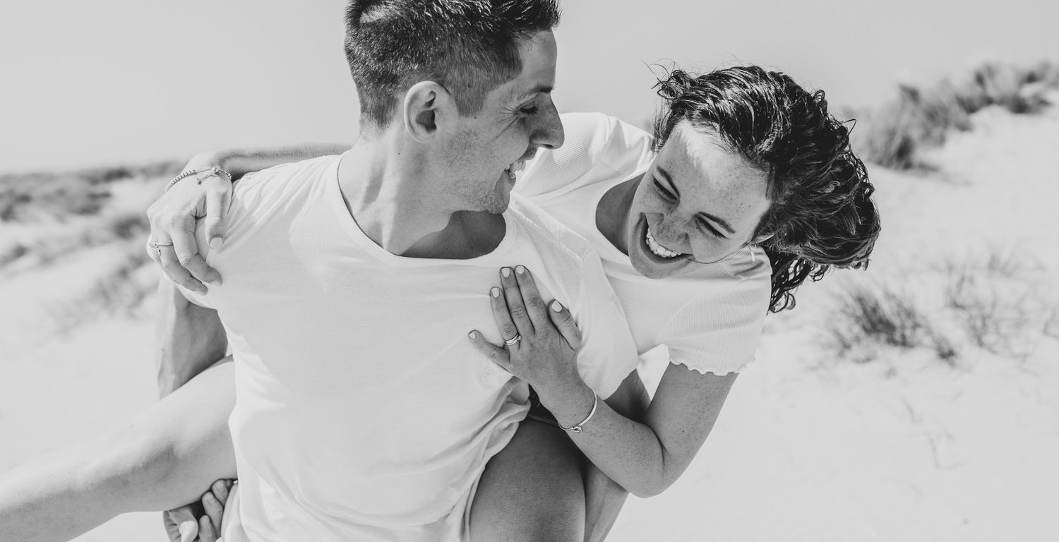 Black and white photo of playful couple on sand dunes.