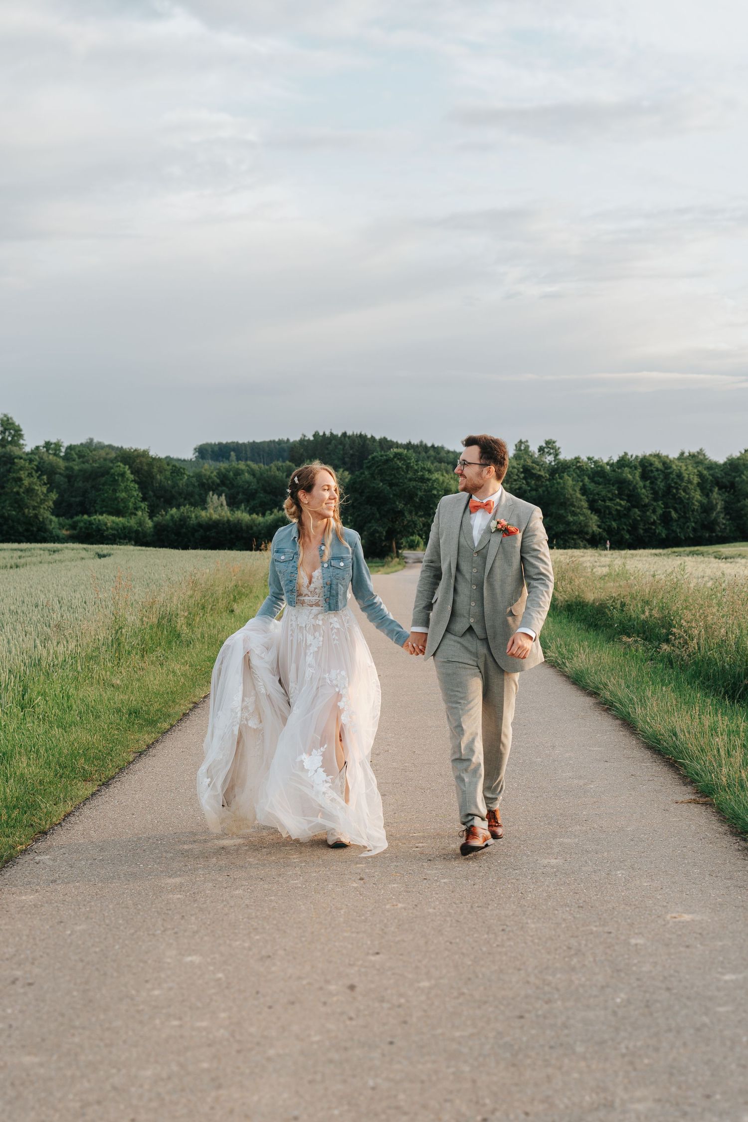 A romantic couple embraces in a golden wheat field under cloudy skies wearing wedding attire.