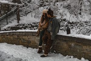 Couple embracing in a snowy winter scene against a stone wall.