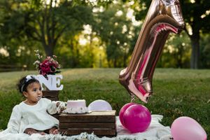 First birthday party setup with pink balloons, cake, and decorations in an outdoor garden setting.