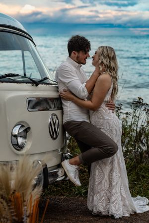 Romantic couple embracing against a vintage VW van at sunset by the ocean.