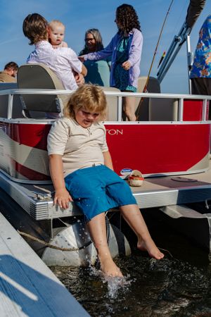 Child splashing water from pontoon boat on sunny summer day.