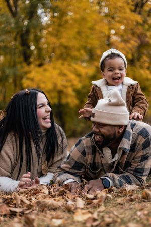 Family laughing together while lying in fallen autumn leaves.