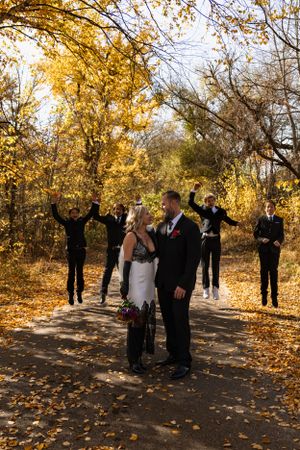 Wedding ceremony on a path covered in golden autumn leaves with celebrating guests in the background.