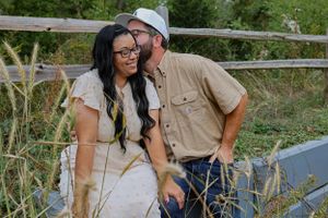 Candid moment of a couple laughing together on a rustic wooden fence.