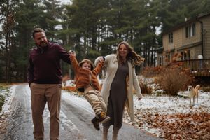 Family playing together in the driveway path swinging child between them.