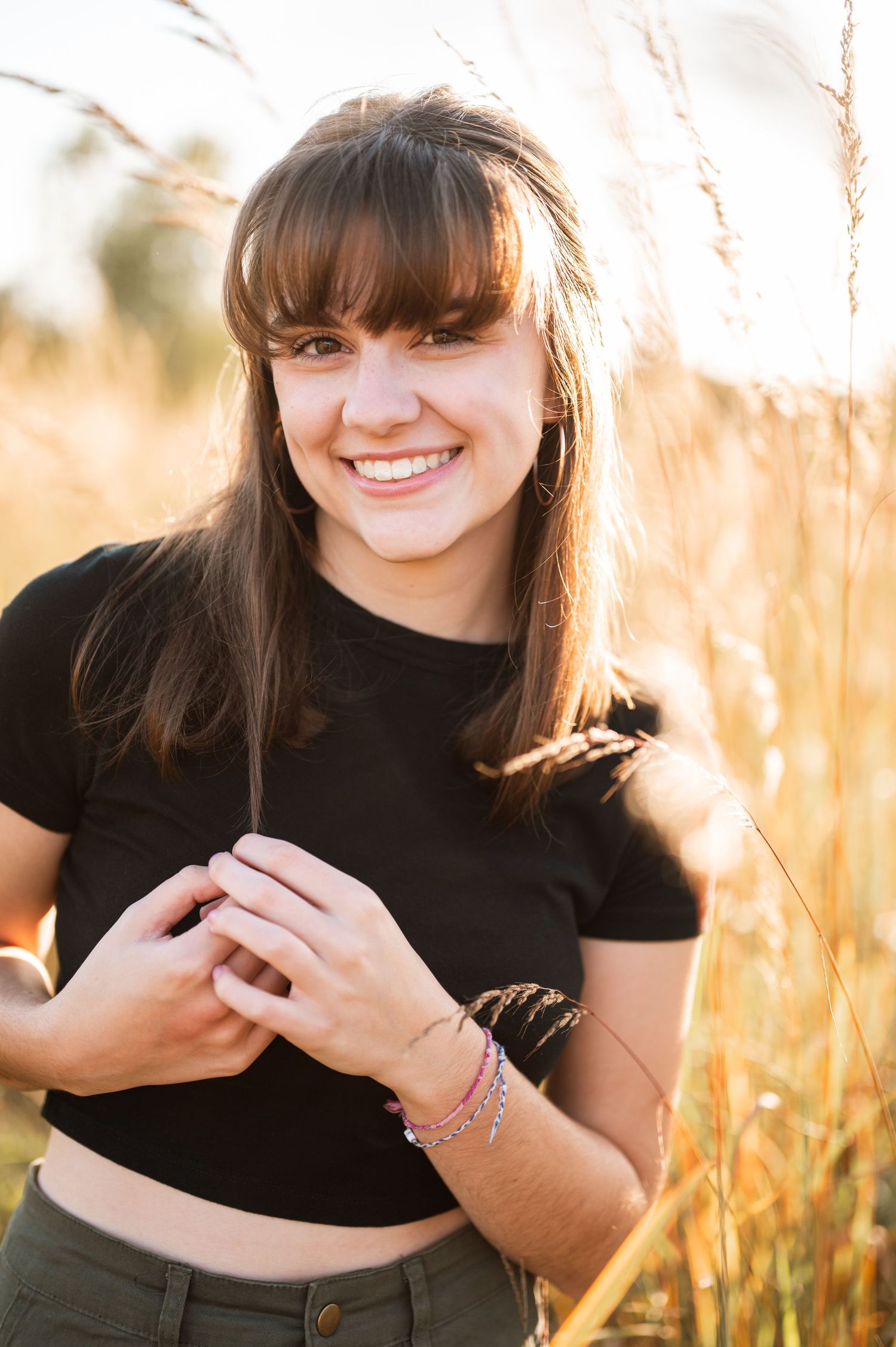 Portrait of woman in black top smiling in golden sunlit field.