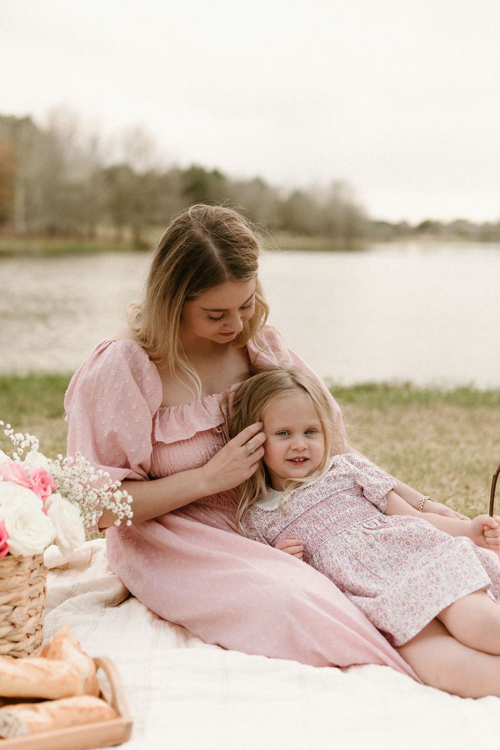 Intimate picnic scene by the water with pink dresses and floral arrangements.