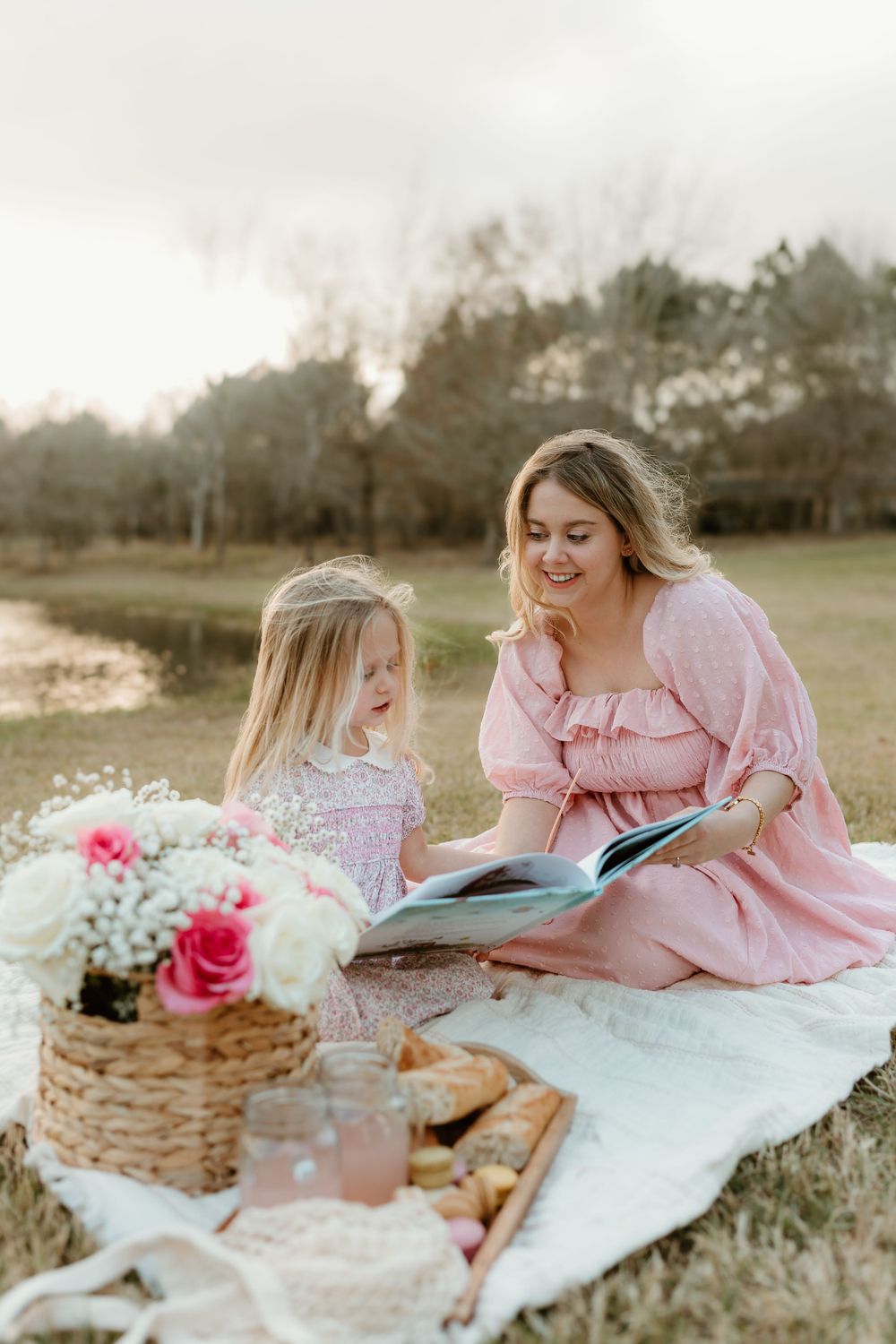 Reading together on a picnic blanket with flowers and a woven basket by the lake.