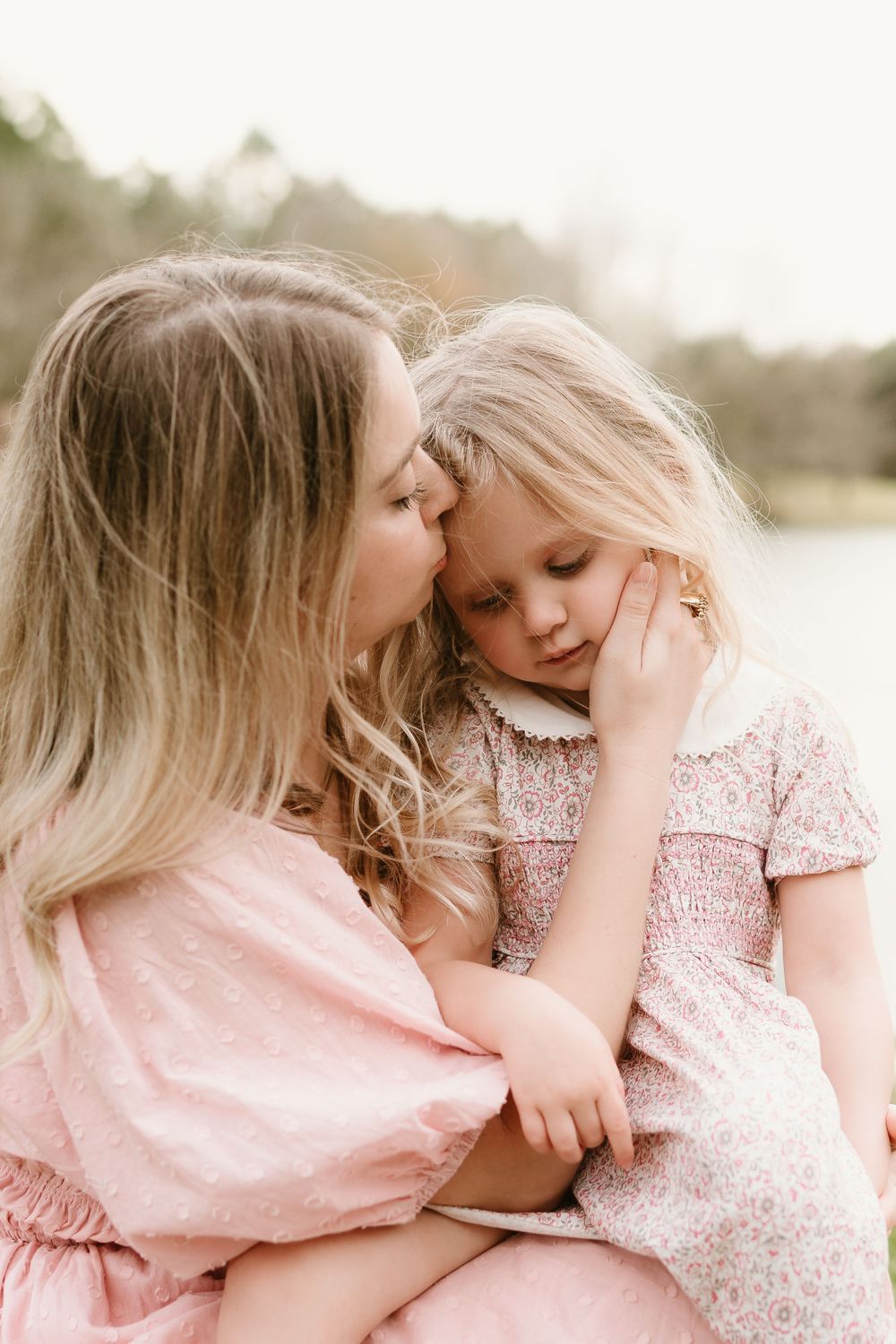 Tender embraces captured in soft pink tones during lakeside photoshoot.