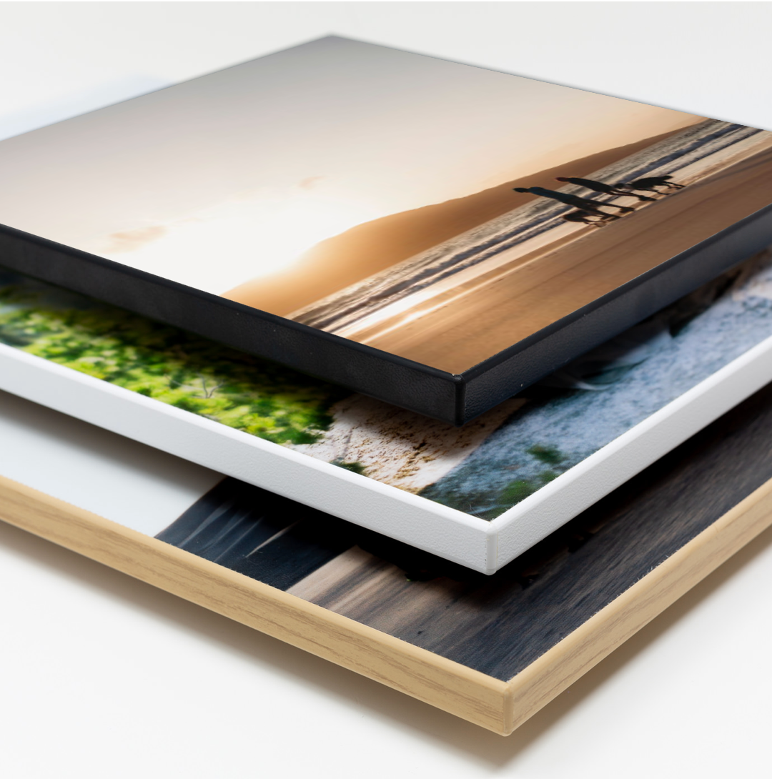 Stack of mounted photographic prints showing layered images of landscapes and nature scenes on different substrates.