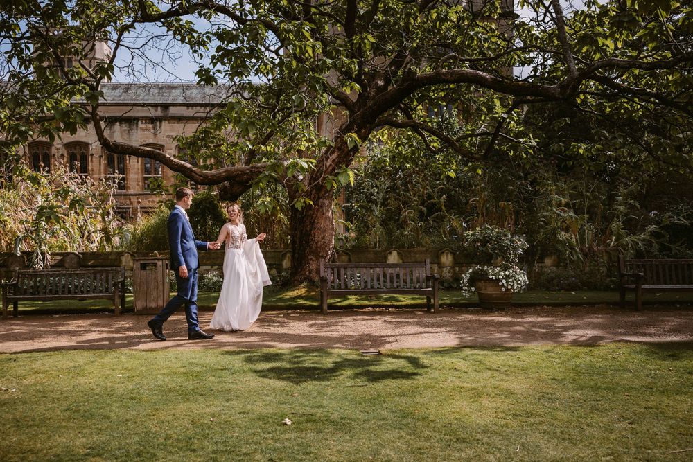 A wedding couple stands together on manicured grounds with historic architecture in the background at Balliol College, Oxford