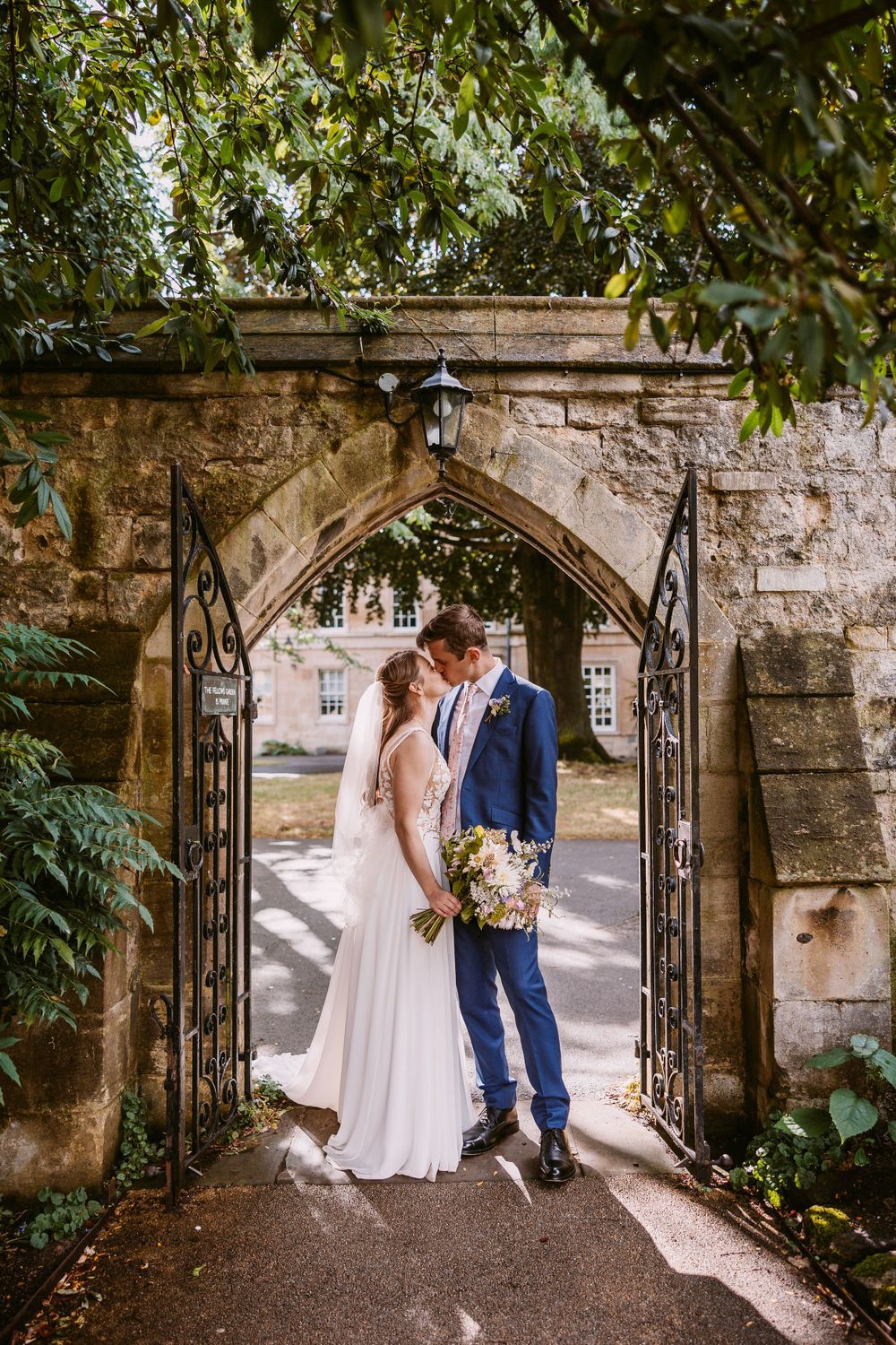 A wedding couple shares an intimate moment under a gothic stone archway with intricate ironwork at Balliol College, Oxford