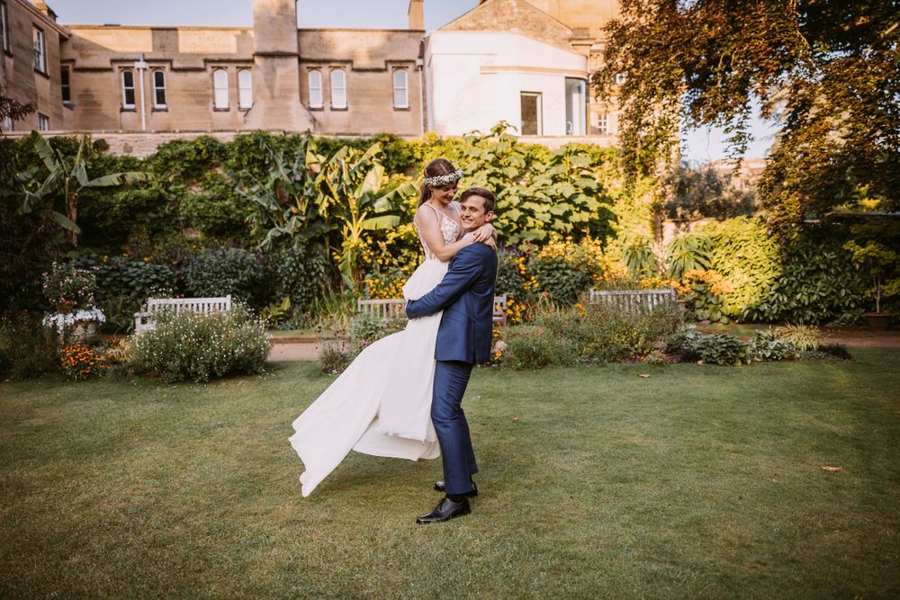 A romantic lift pose in a manicured garden with historic buildings in the background during golden hour.