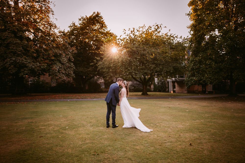 A wedding couple stands on a lawn at sunset with autumn trees in the background at Balliol College, Oxford