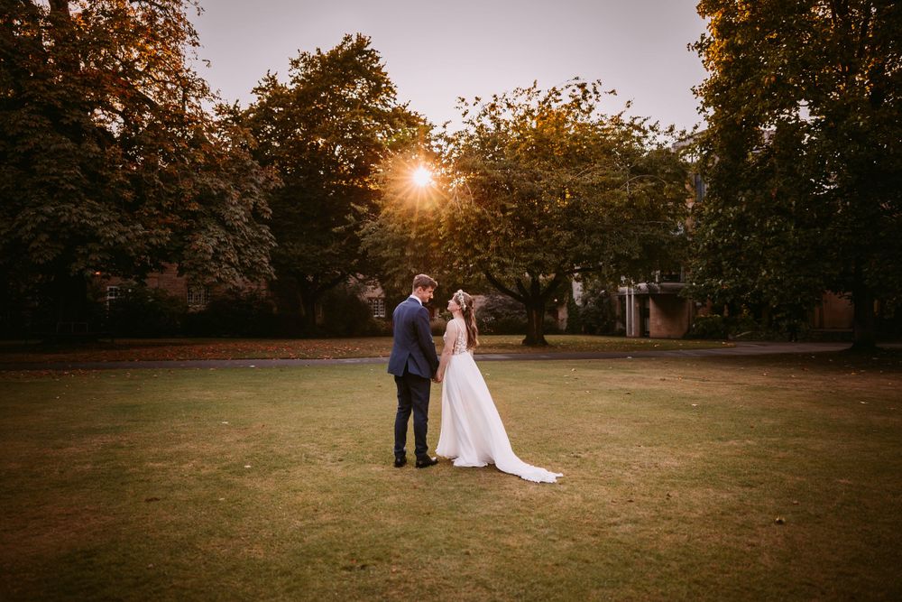 A romantic sunset wedding portrait shows a couple embracing on a grassy lawn surrounded by fall foliage.