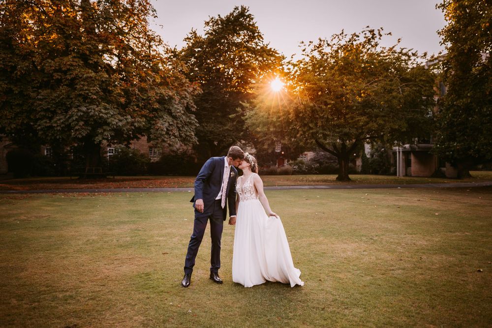 A sunset wedding photo captures a couple's intimate moment on a lawn surrounded by autumn trees at Balliol College, Oxford