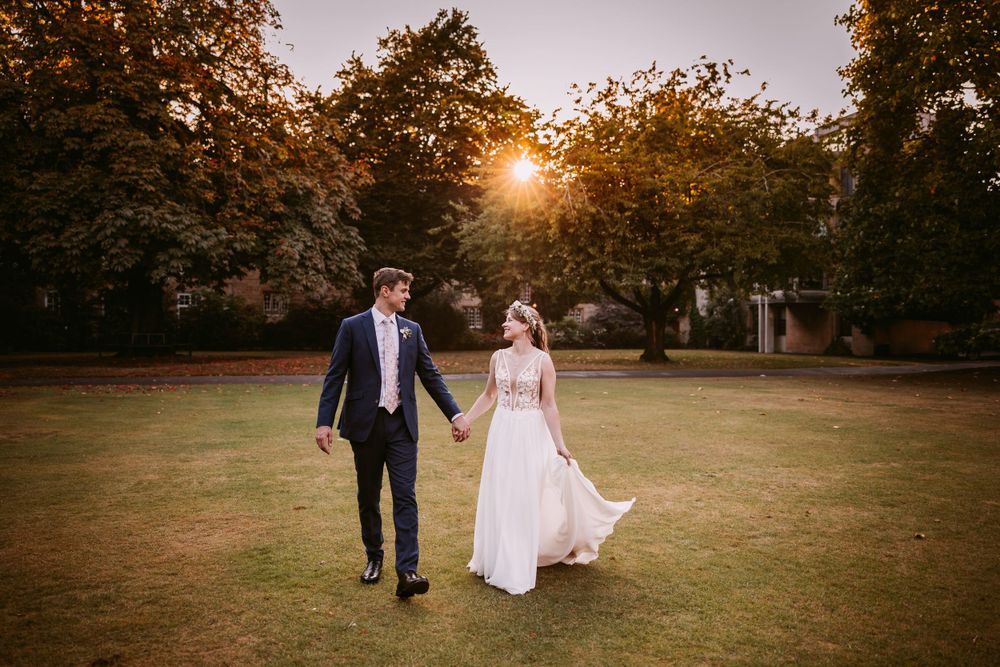 Newlyweds walk hand in hand across a golden sunlit lawn during their autumn wedding at Balliol College, Oxford