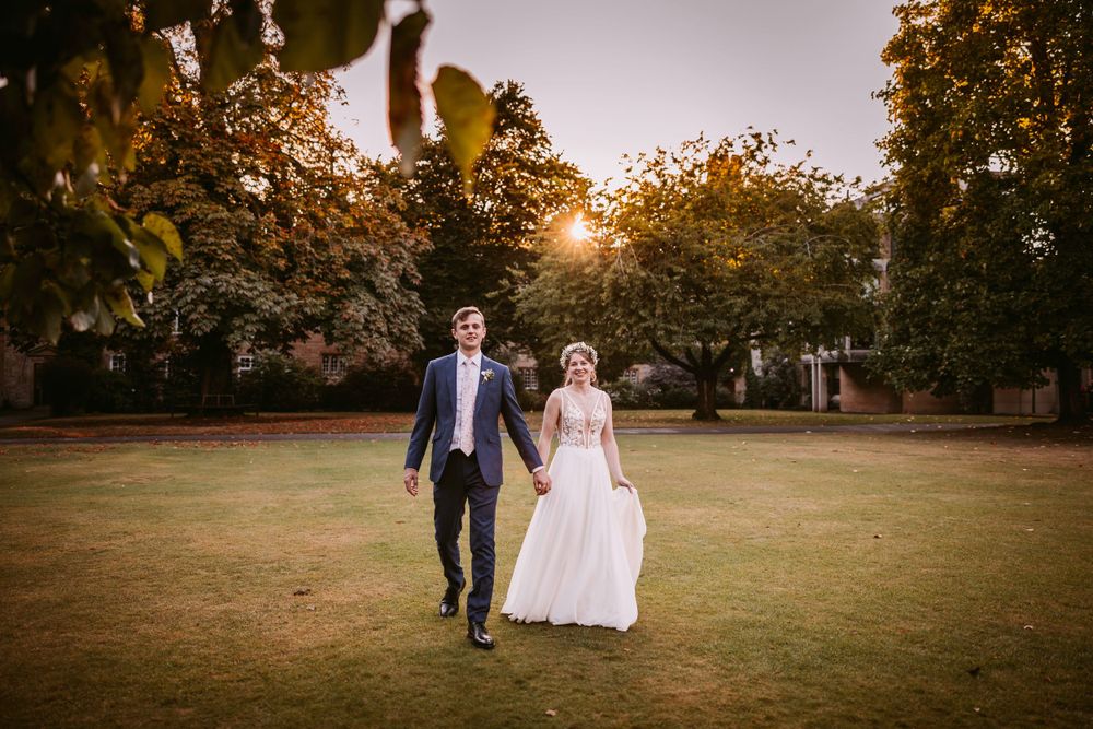 Joyful young bride and groom weds run across a sunlit lawn during their autumn wedding celebration at Balliol College, Oxford