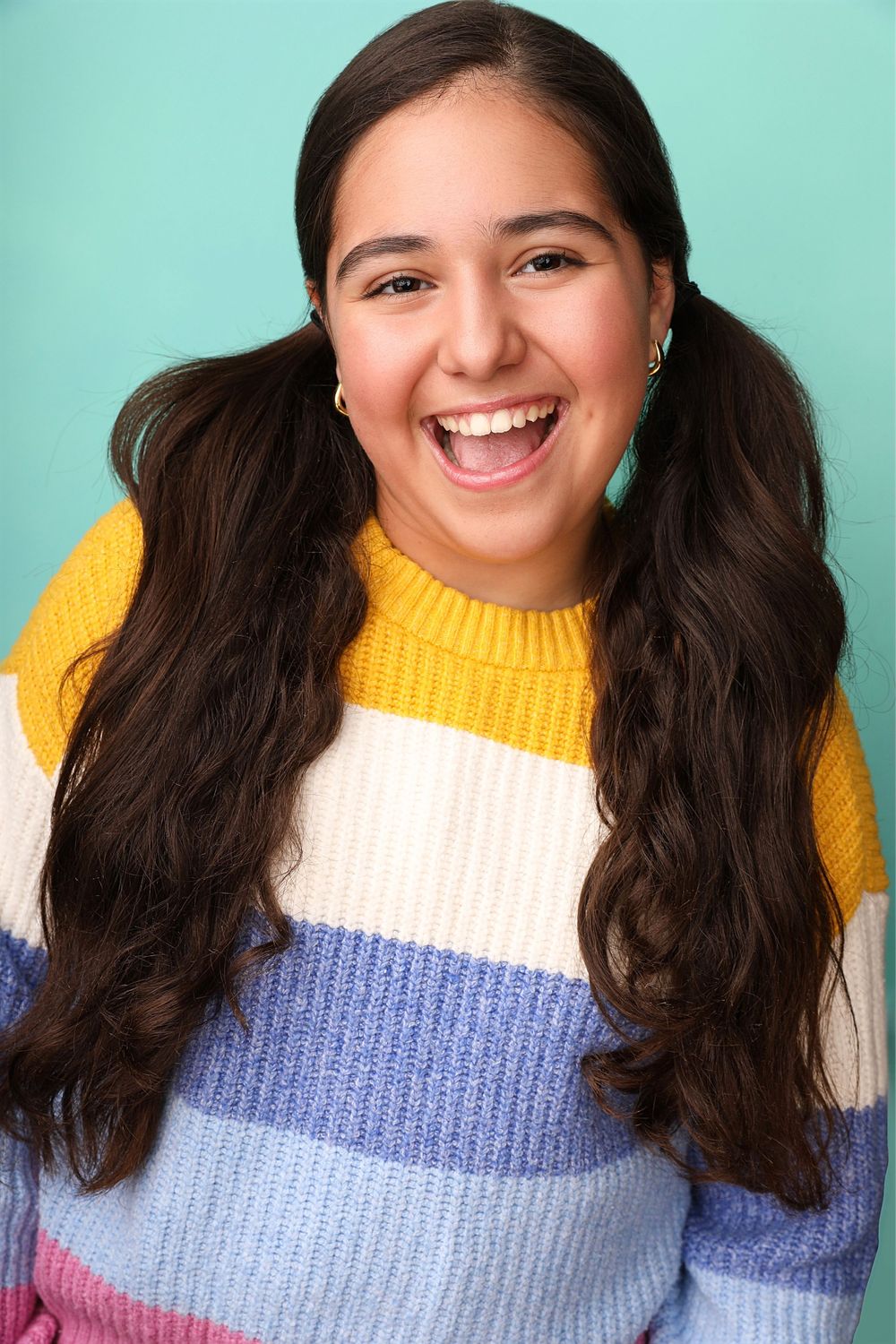 A cheerful young woman in a colorful striped sweater laughs against a turquoise background.