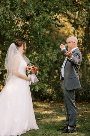 A wedding couple shares a candid moment outdoors surrounded by autumn trees.