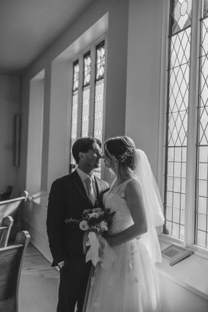 A romantic wedding moment captured in black and white by ornate church windows.