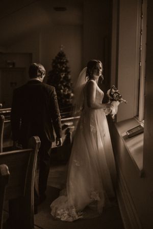 A silhouetted wedding couple stands by a window with a Christmas tree in the background.
