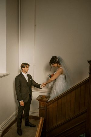 A tender wedding moment captured on a wooden staircase in muted tones.