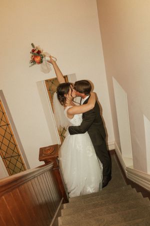 A joyful wedding couple shares a dramatic dip and kiss on a staircase.