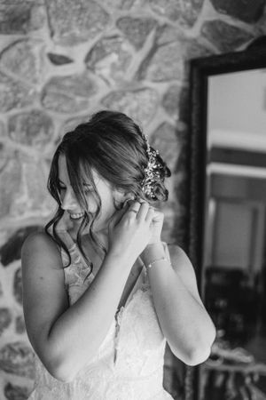 Black and white portrait of bride adjusting earrings against stone wall.